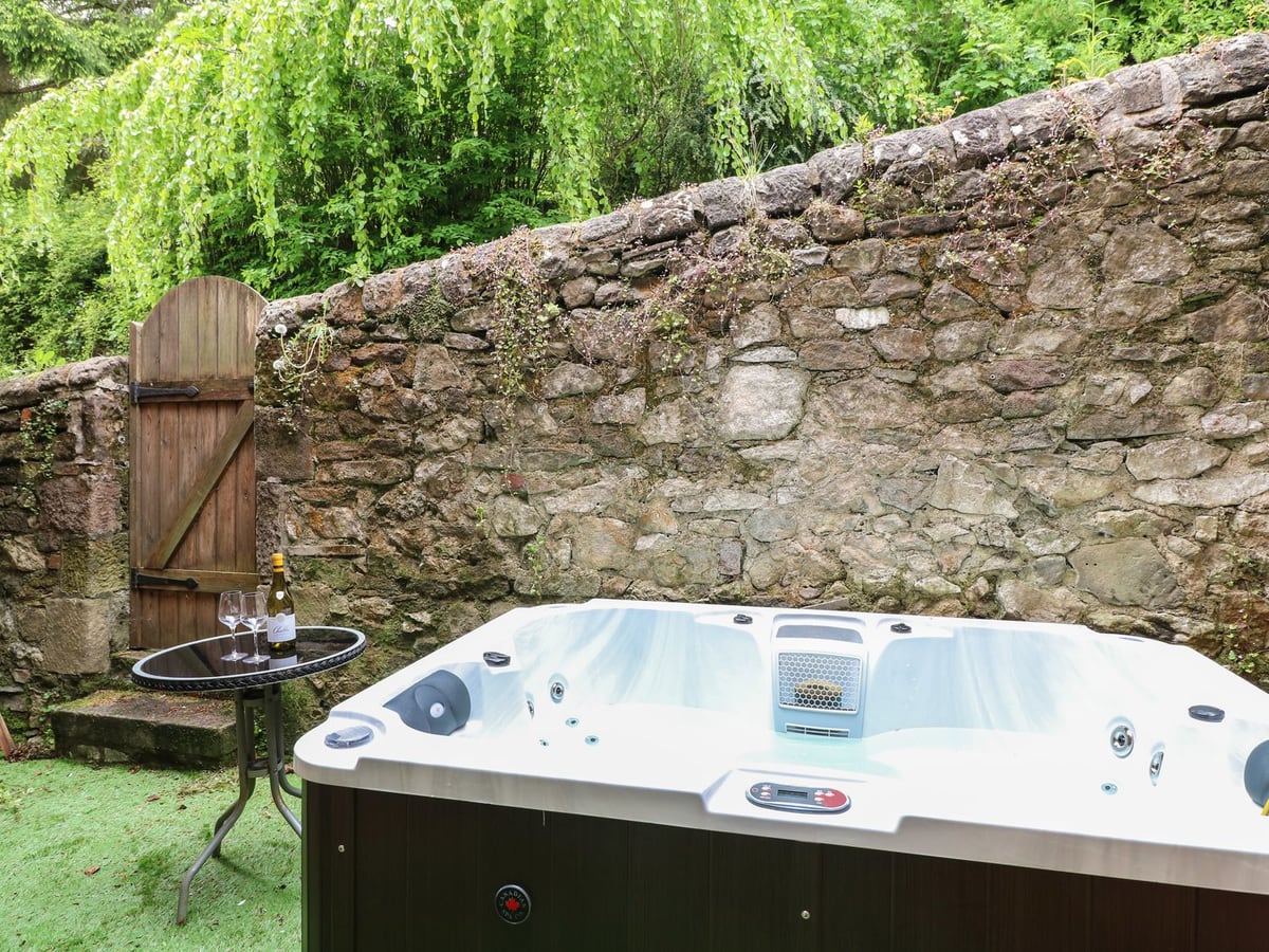 Hot tub beside a stone wall, wooden gate and small round table in the Kirkham House courtyard