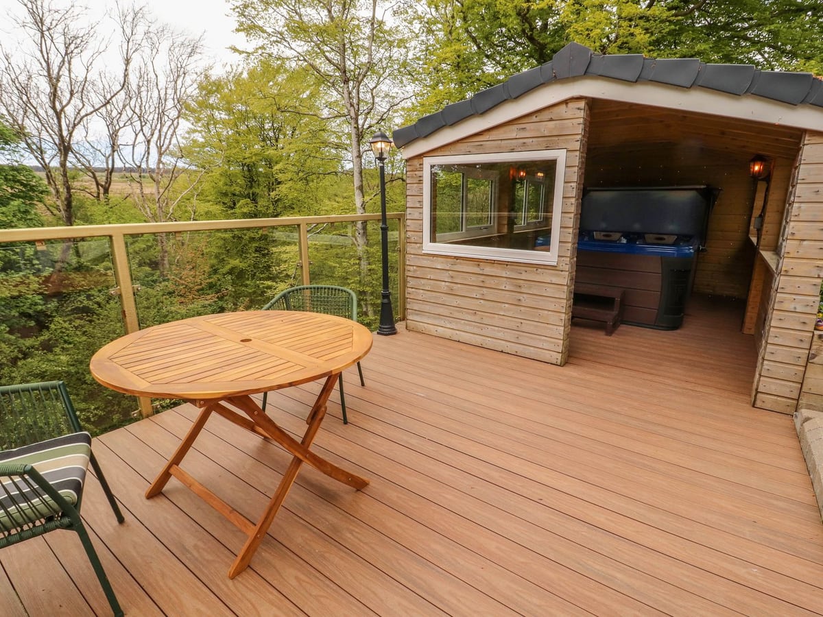 Decking and a round table beside the timber hot-tub shelter at Kirkland Howe Cottage