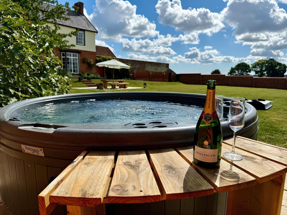 Wood-fired hot tub with the house and garden beyond at Knights Farm