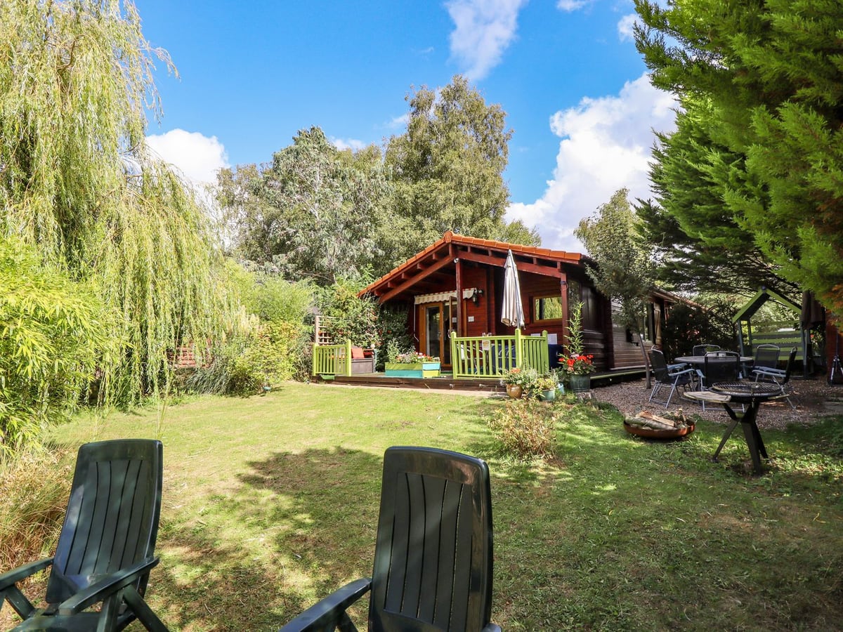 Lakeside Lodge Retreat behind a lawn with willow branches and outdoor seating