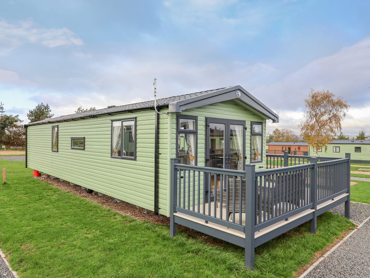 Pale green exterior of Lazy Dayz Lodge with a front deck, grey railings and surrounding grass