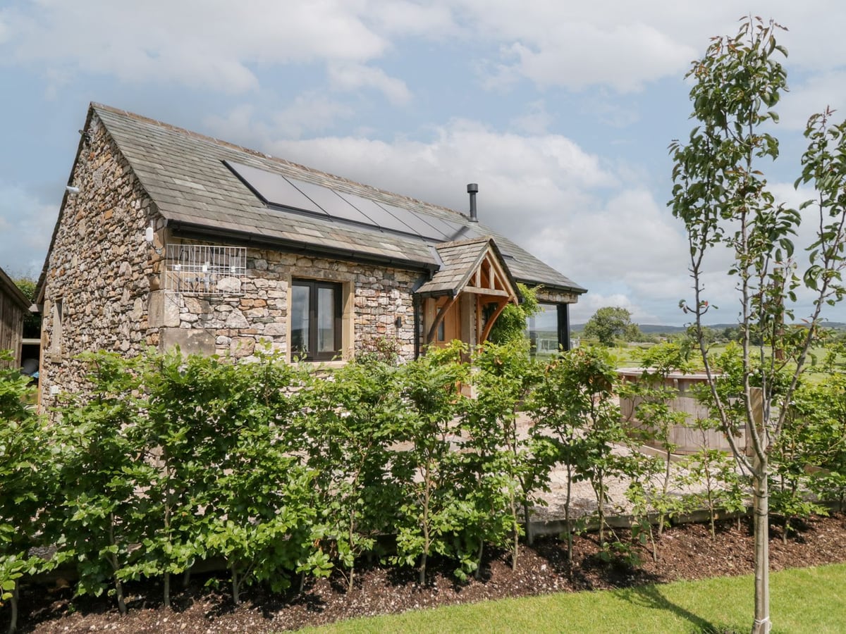 Lindeth Croft stone cottage with a timber porch, planted border and countryside beyond
