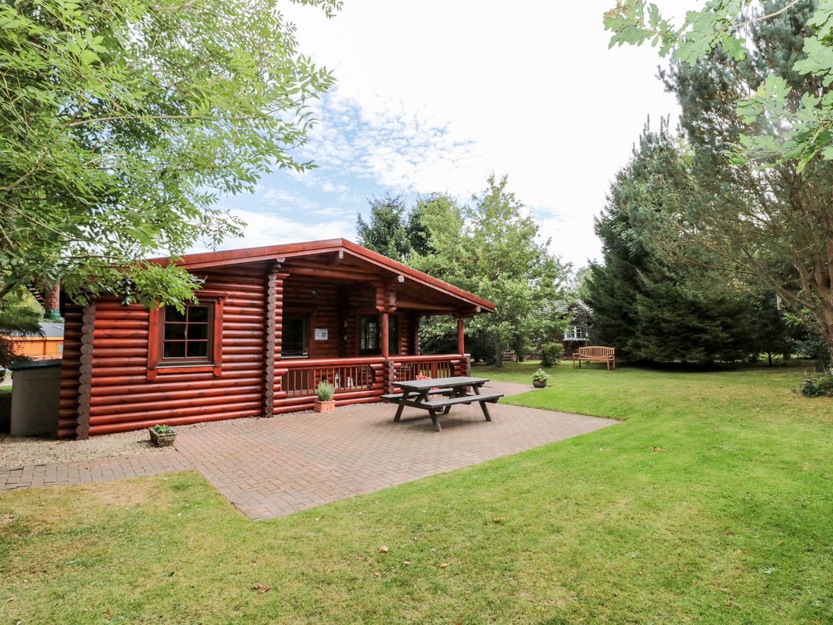 Log cabin, picnic table and lawn at Little Bears Hideaway, surrounded by mature trees.