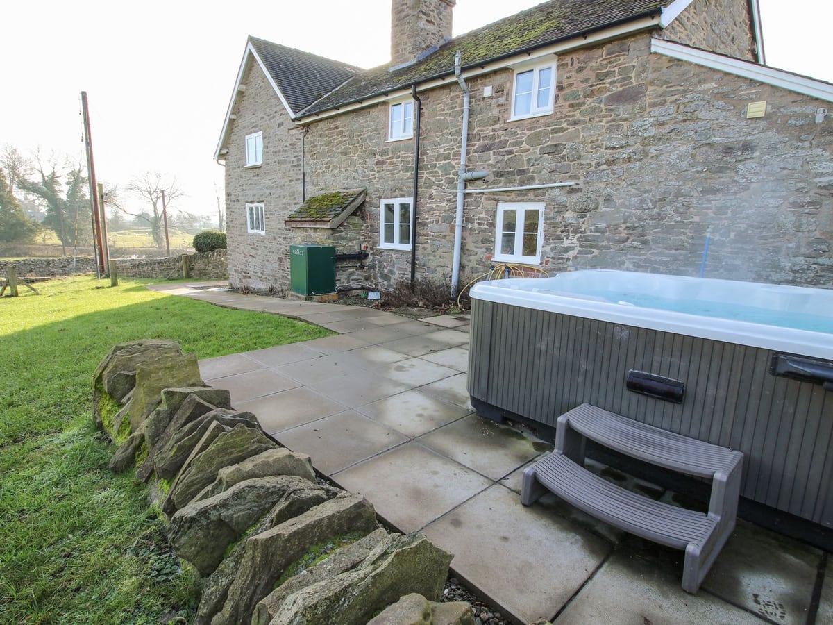 Hot tub beside Little Bicton's stone walls, paved terrace, low stone edging and lawn
