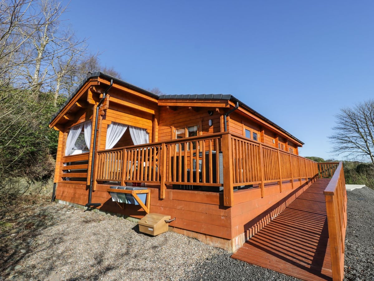 Little Lodge timber cabin with a raised veranda, access ramp and gravel around the building