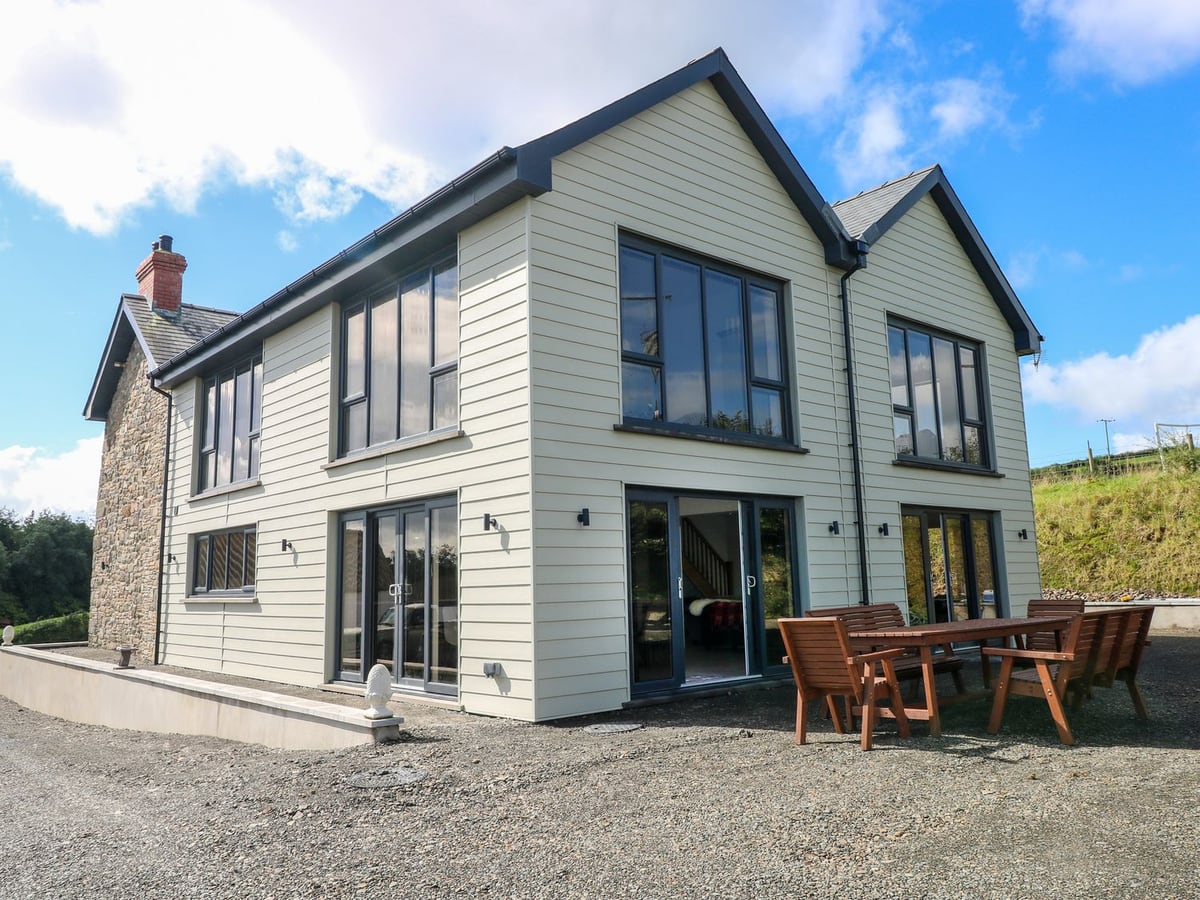 Little Pale, a clad two-storey house with glazed doors, wooden patio table and chairs on gravel