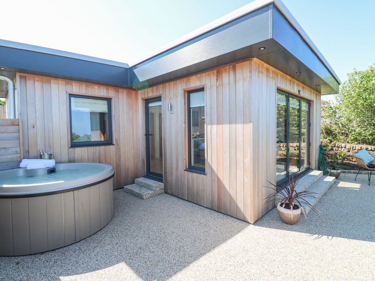 Round hot tub beside Little Victory's timber exterior, with a gravel terrace and glass doors