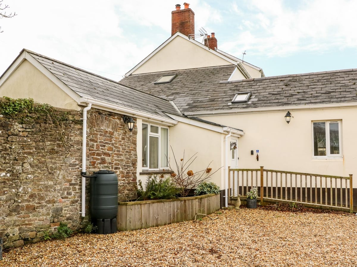 Cream and stone cottage wing beside a gravel courtyard at Littleham Court Cottage