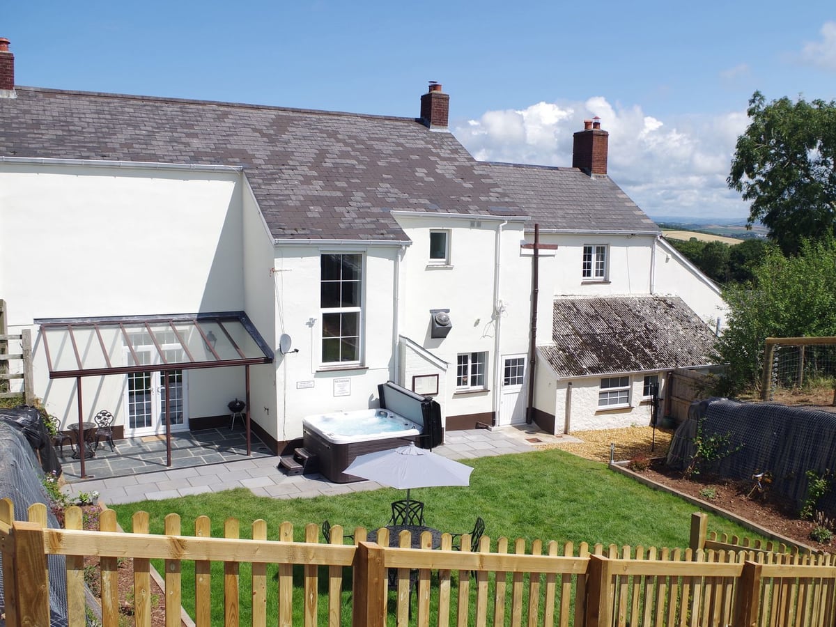 Tall white rear facade beside a lawn, patio and hot tub at Littleham Court Manor