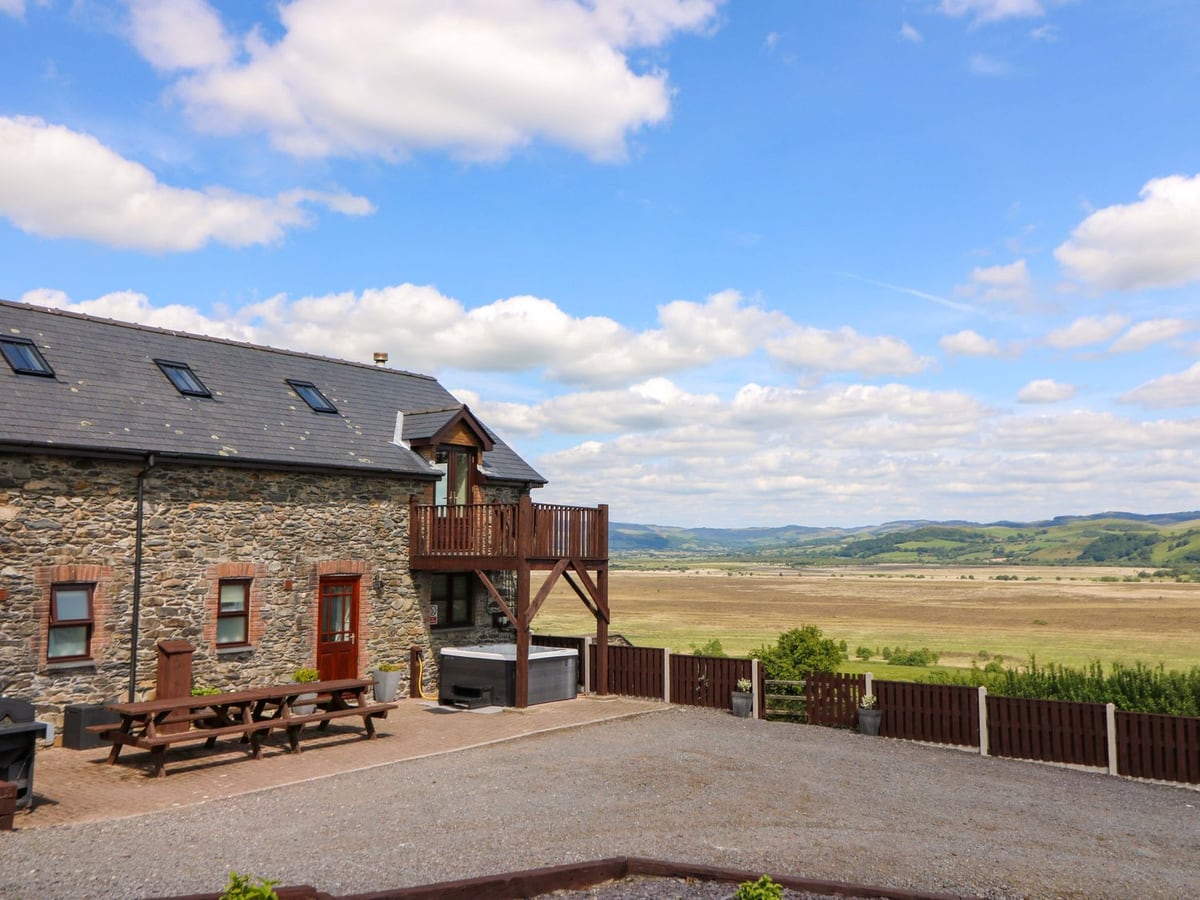 Llwyngwinau Isaf Barn stone exterior with patio benches, a hot tub with its lid on and a wide valley view