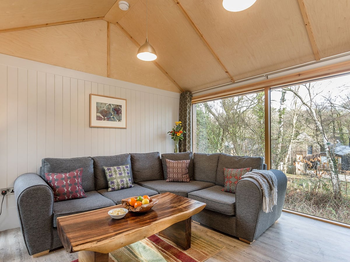 Grey corner sofa in the living room at Lodge 17, with a wooden table and windows onto trees
