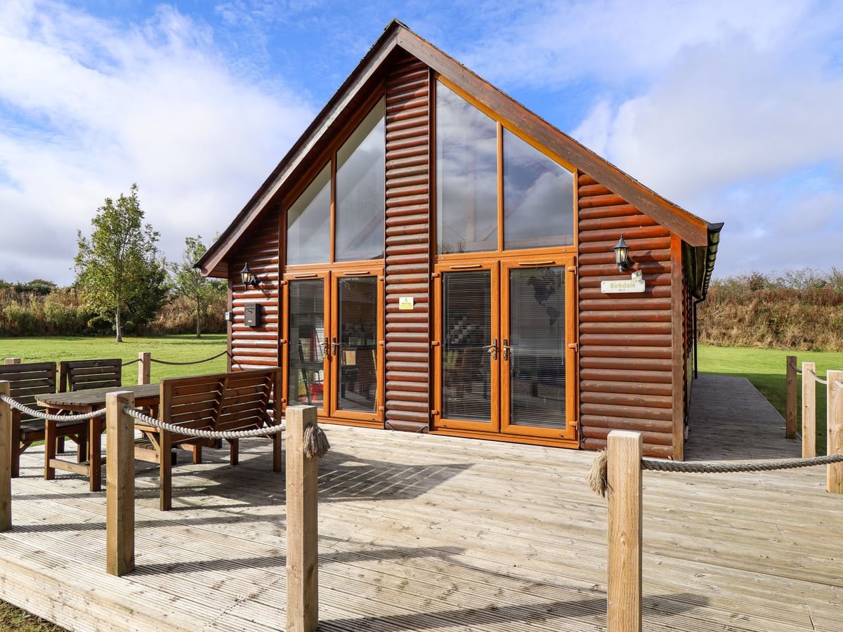 Glazed gable of Lodge 3 with timber decking, rope rails and an outdoor dining table