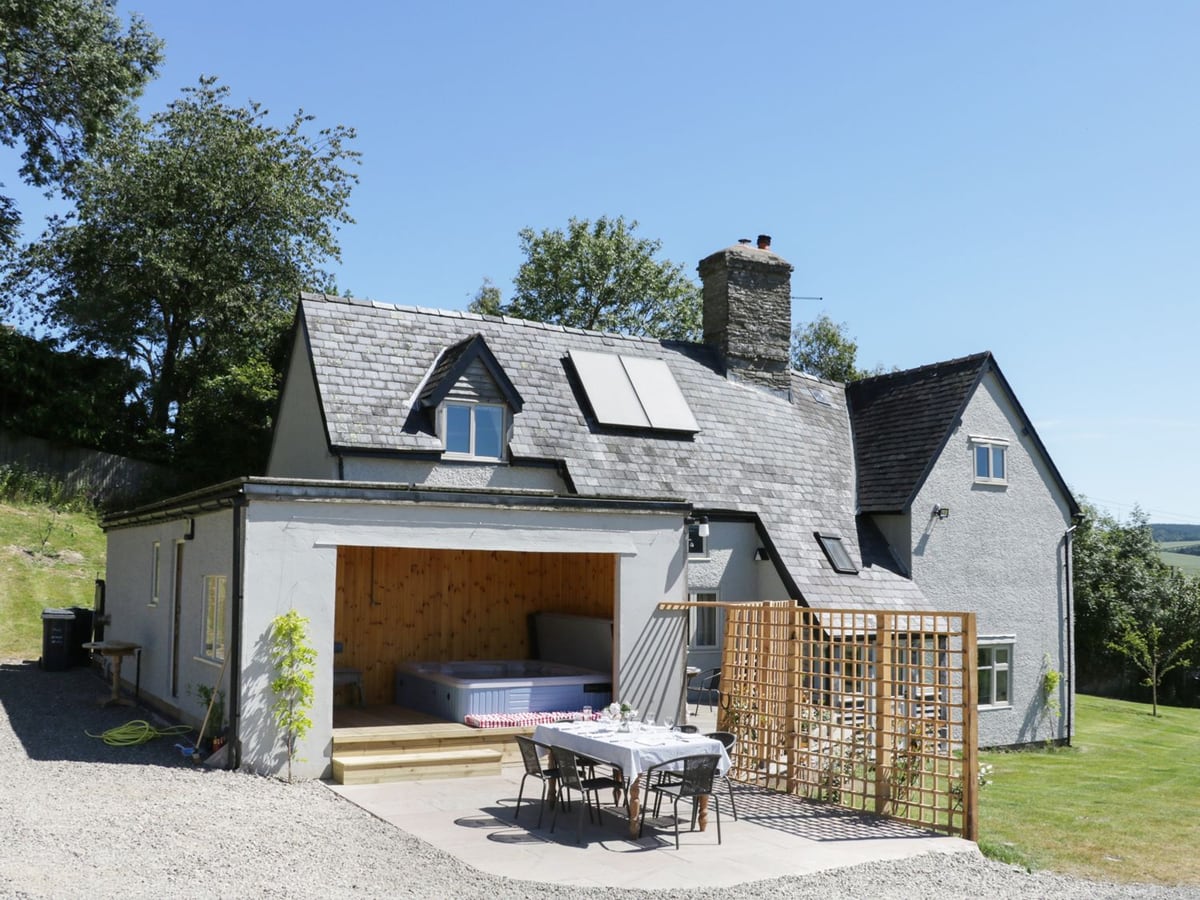Lower Hodre's white exterior with a sheltered hot tub, dining terrace and sloping lawn