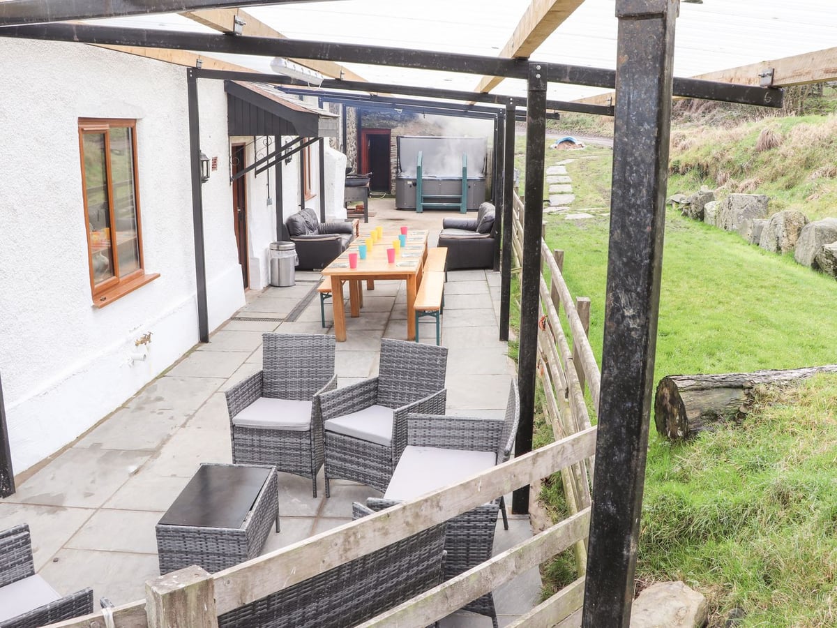 Covered patio at Maestyddyn Farm House with wicker seating, a long dining table and a hot tub at the far end