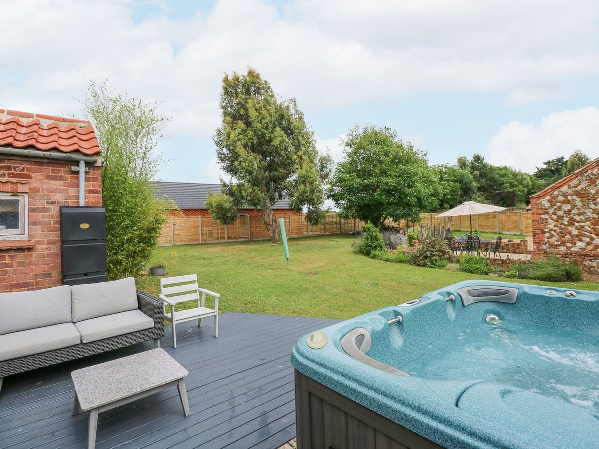 Hot tub and outdoor seating overlooking the lawn and trees at Malthouse Farm in Heacham