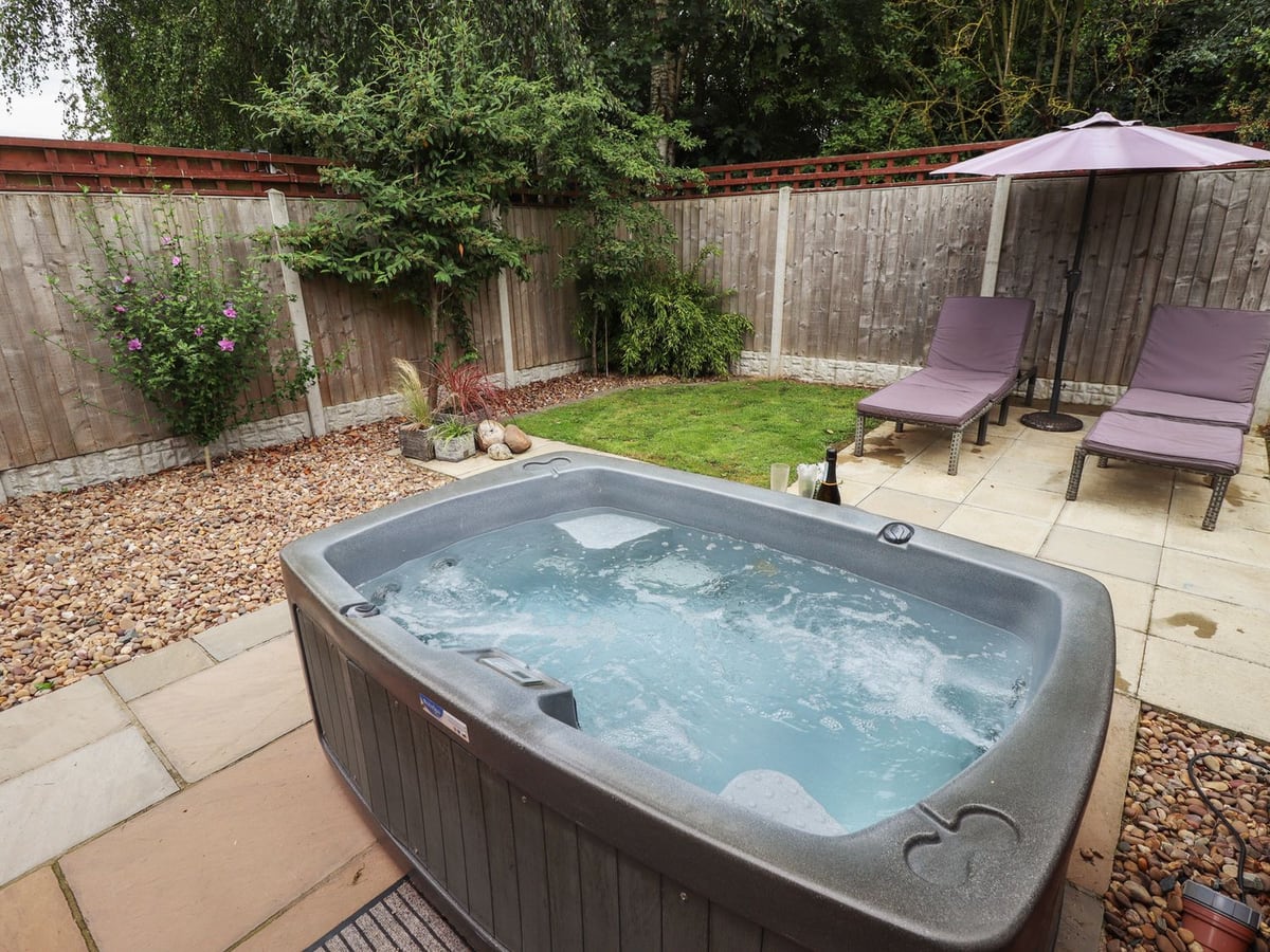Hot tub beside lawn and two loungers in Marsh View Cottage's rear garden