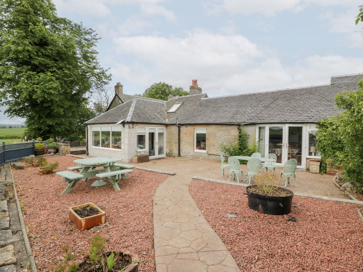 Marshill Farm House with a gravel courtyard, outdoor tables and trees beside the stone building