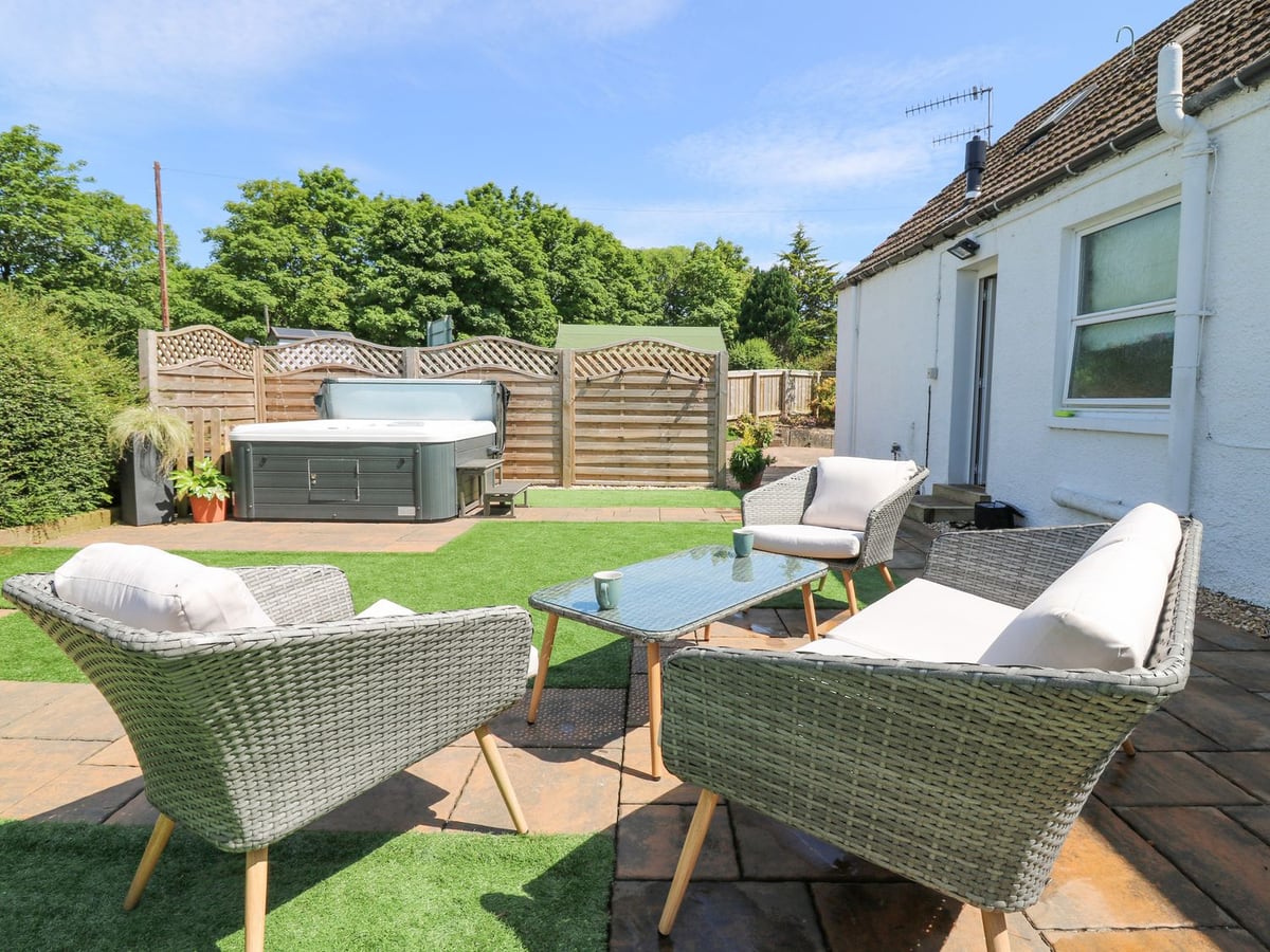 Rear patio seating, artificial turf and hot tub beside the white walls of Maryland Cottage