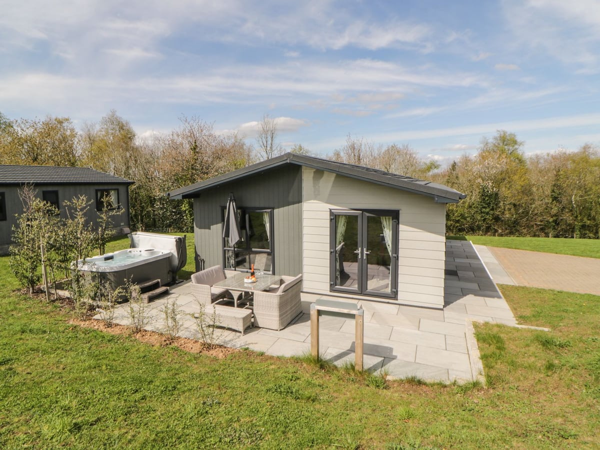 Pale lodge with glazed doors beside patio furniture and a hot tub at Meadow Lodge