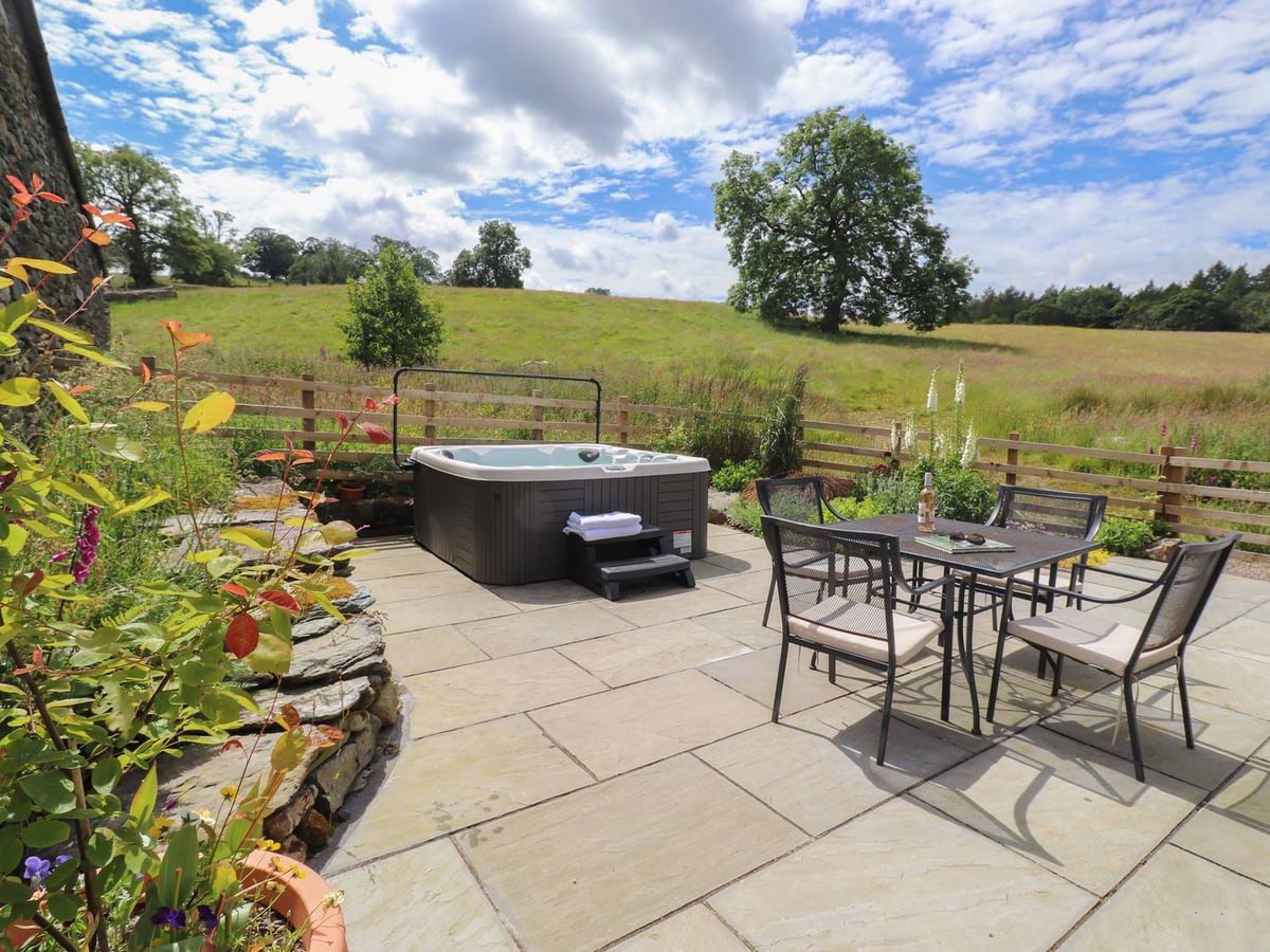 Hot tub and patio table beside planted borders and a wooden fence at Meadow Syke Barn