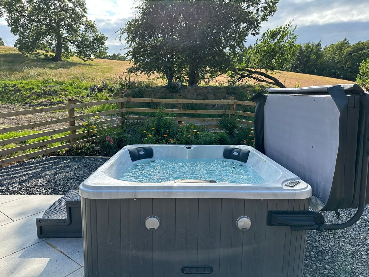 Meadow Syke Byre hot tub beside slate gravel, a wooden fence and planted borders