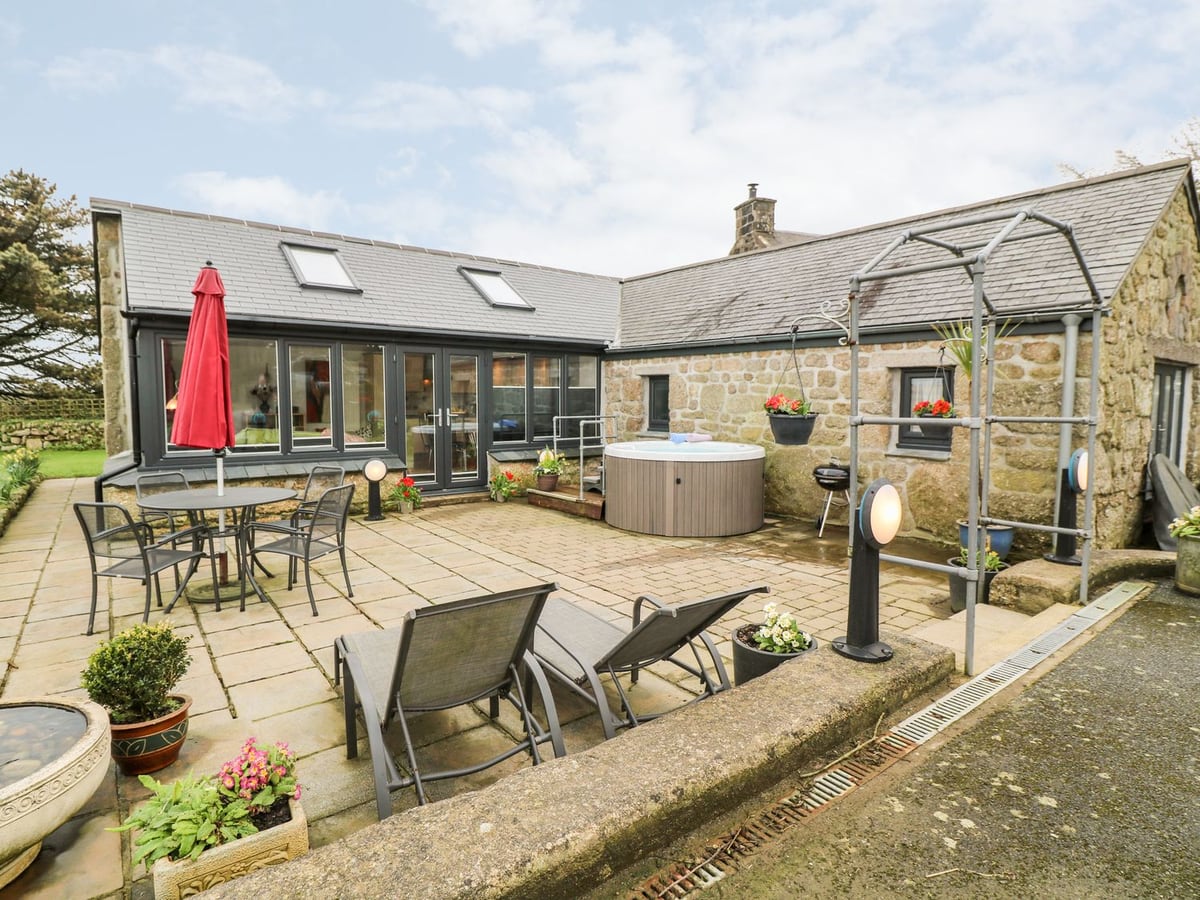 Meadowside's stone exterior and glazed living room beside a patio, round hot tub and loungers