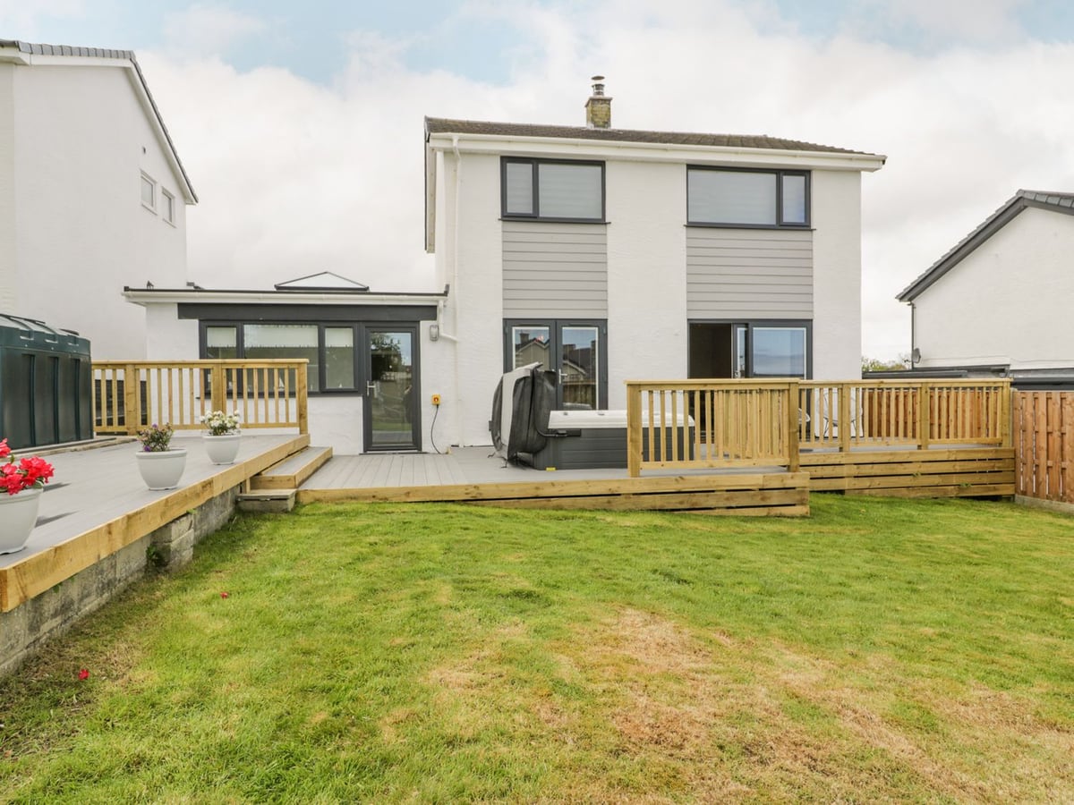 Melody lawn and multi-level decking with rails and a hot tub with its lid raised, white house behind