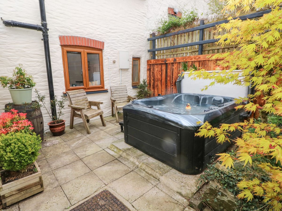 Mill Barn Denant paved patio with a hot tub with its lid folded back, two wooden chairs and planters