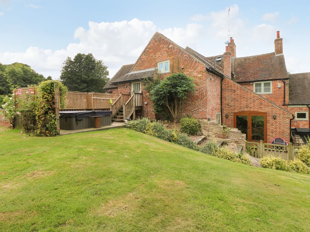 Mill Farm The Farmhouse with a sloping lawn, red brick walls and hot tub beside a raised deck