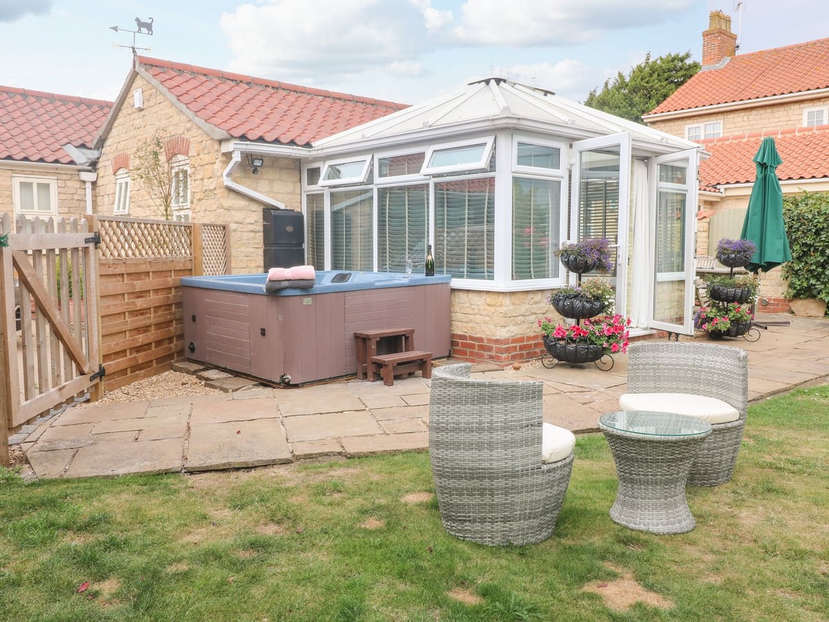 Millcott's conservatory beside a hot tub patio, potted flowers and lawn seating