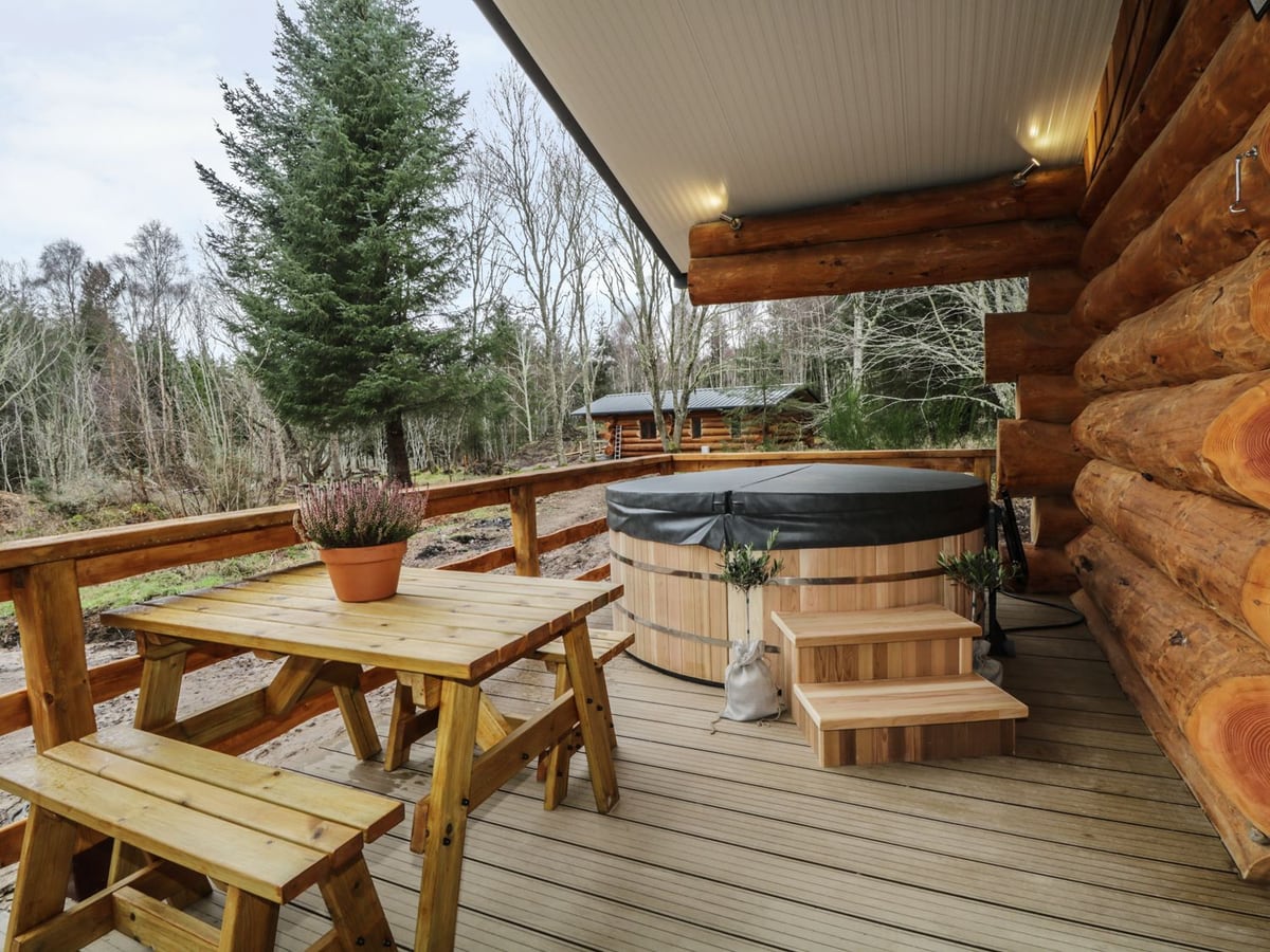 Covered hot tub and picnic table on Moorhen Lodge veranda, with woodland beyond the railing
