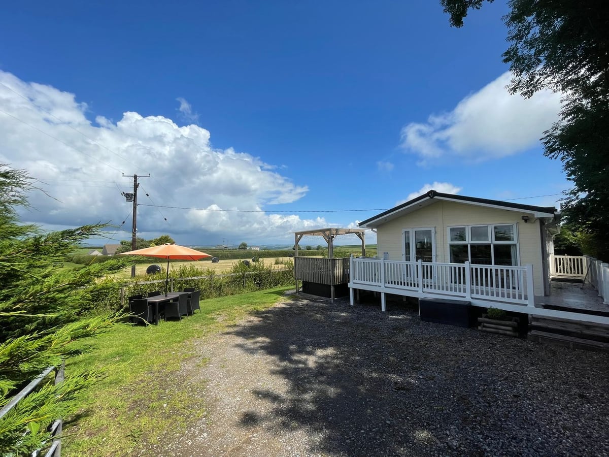 Mountain View Lodge with white-railed decking, a timber gazebo, lawn dining set and farmland beyond