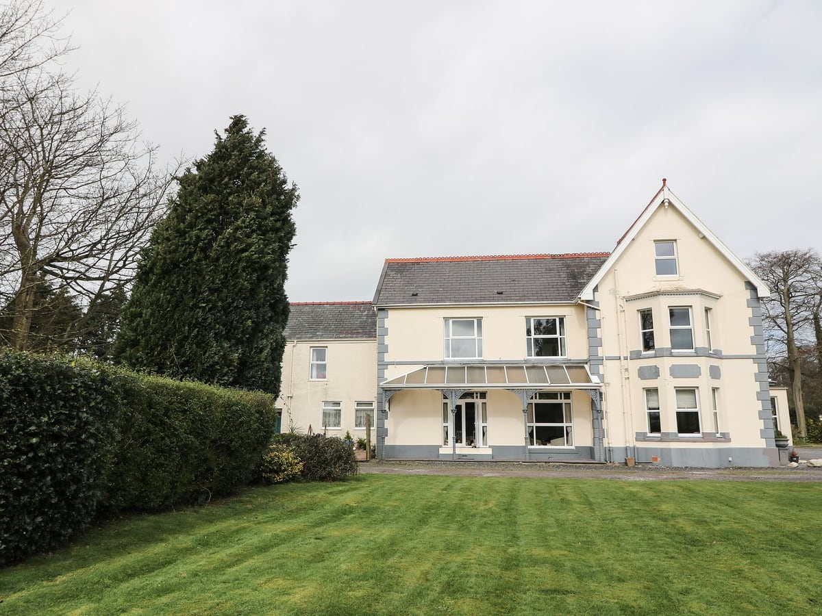 Muriau Park, a large cream house with a glass veranda, beside a hedge and wide mown lawn