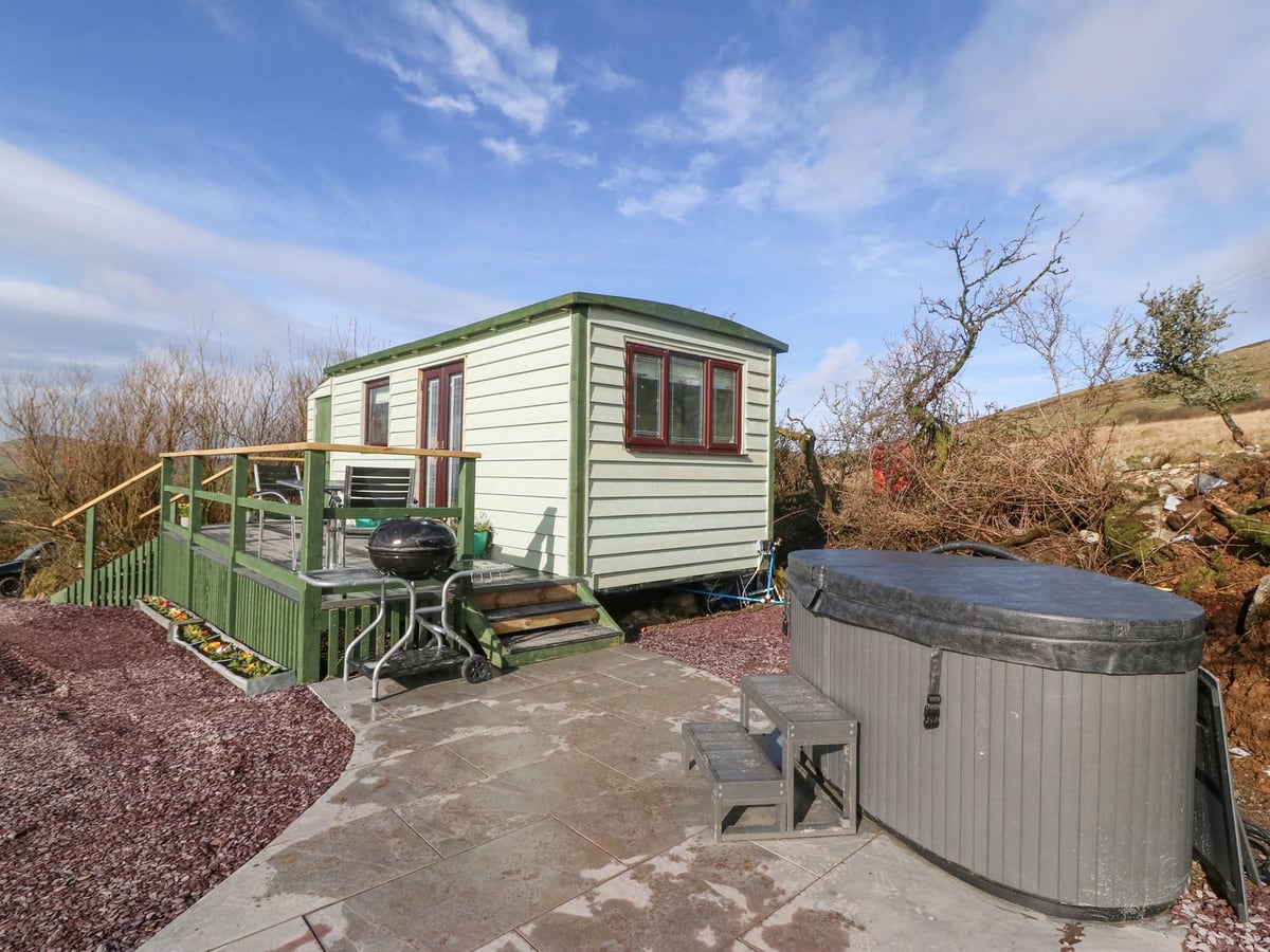 Nyth Y Bioden hut with a railed deck, barbecue and a hot tub with its lid on, on a paved patio