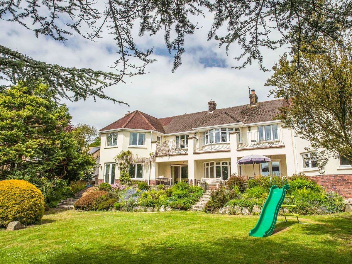 Large cream house with balconies above the planted terrace and garden lawn at Nairn