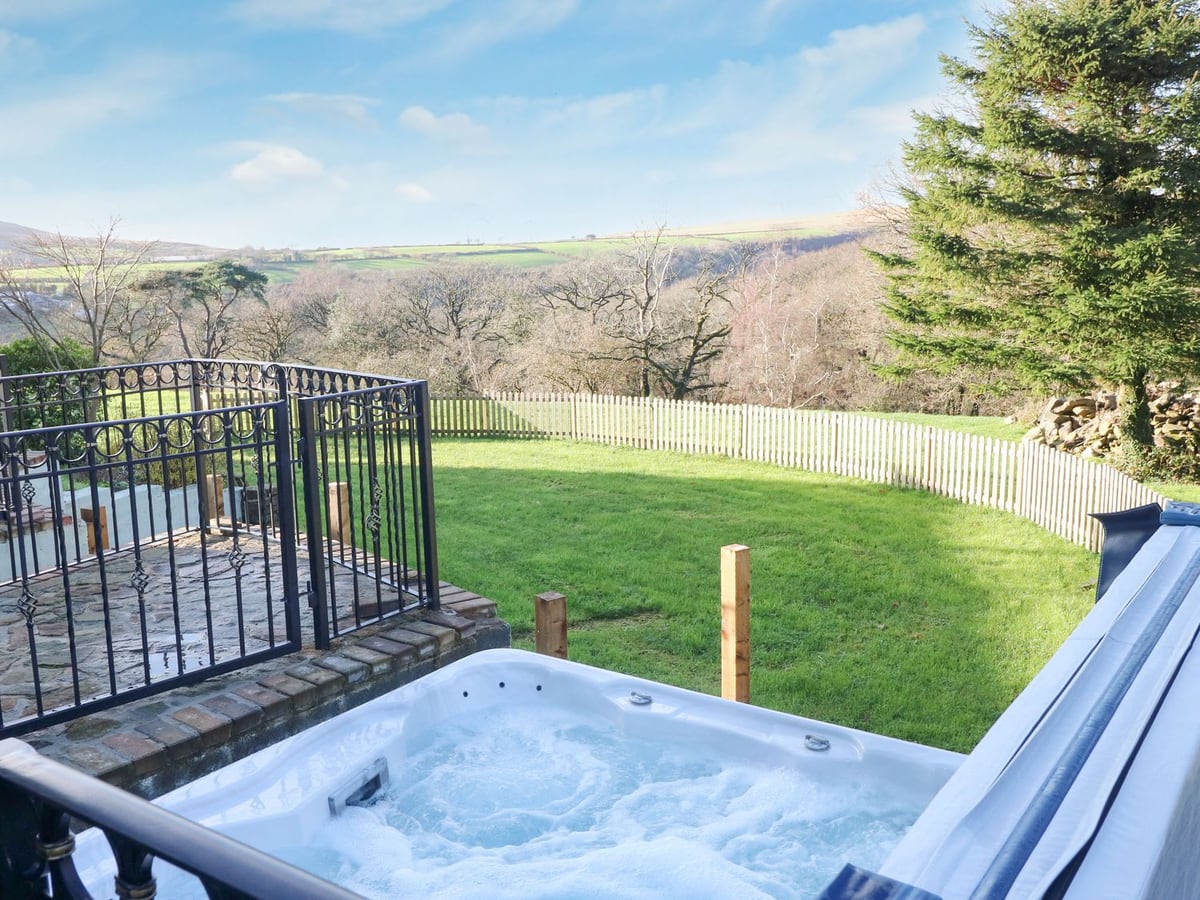 Open hot tub by black railings at Nant Moel Isaf Farm, overlooking a picket-fenced lawn and valley