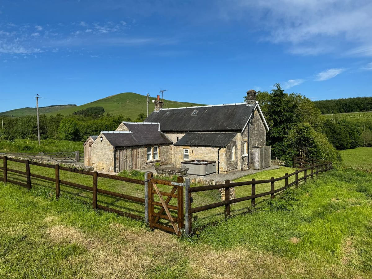 Netherraw stone cottage with a fenced lawn, garden gate and hot tub beside the rear wall