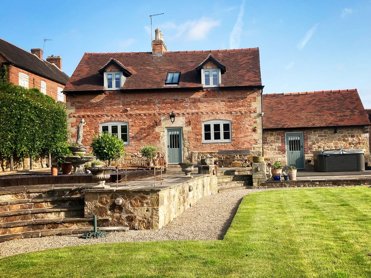 New Elms Farmhouse with a lawn, raised stone patio, steps and a covered hot tub beside the house