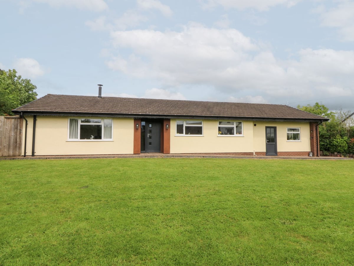 New Peny cream single-storey bungalow with a large mown lawn in front under a cloudy sky