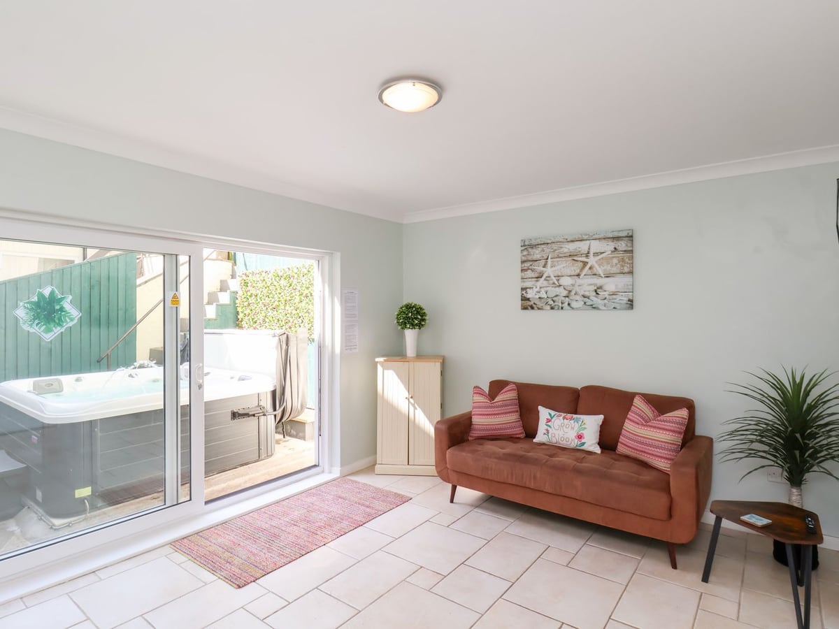 Sitting area with a rust-coloured sofa and sliding doors overlooking the hot tub at North Beach Lodge