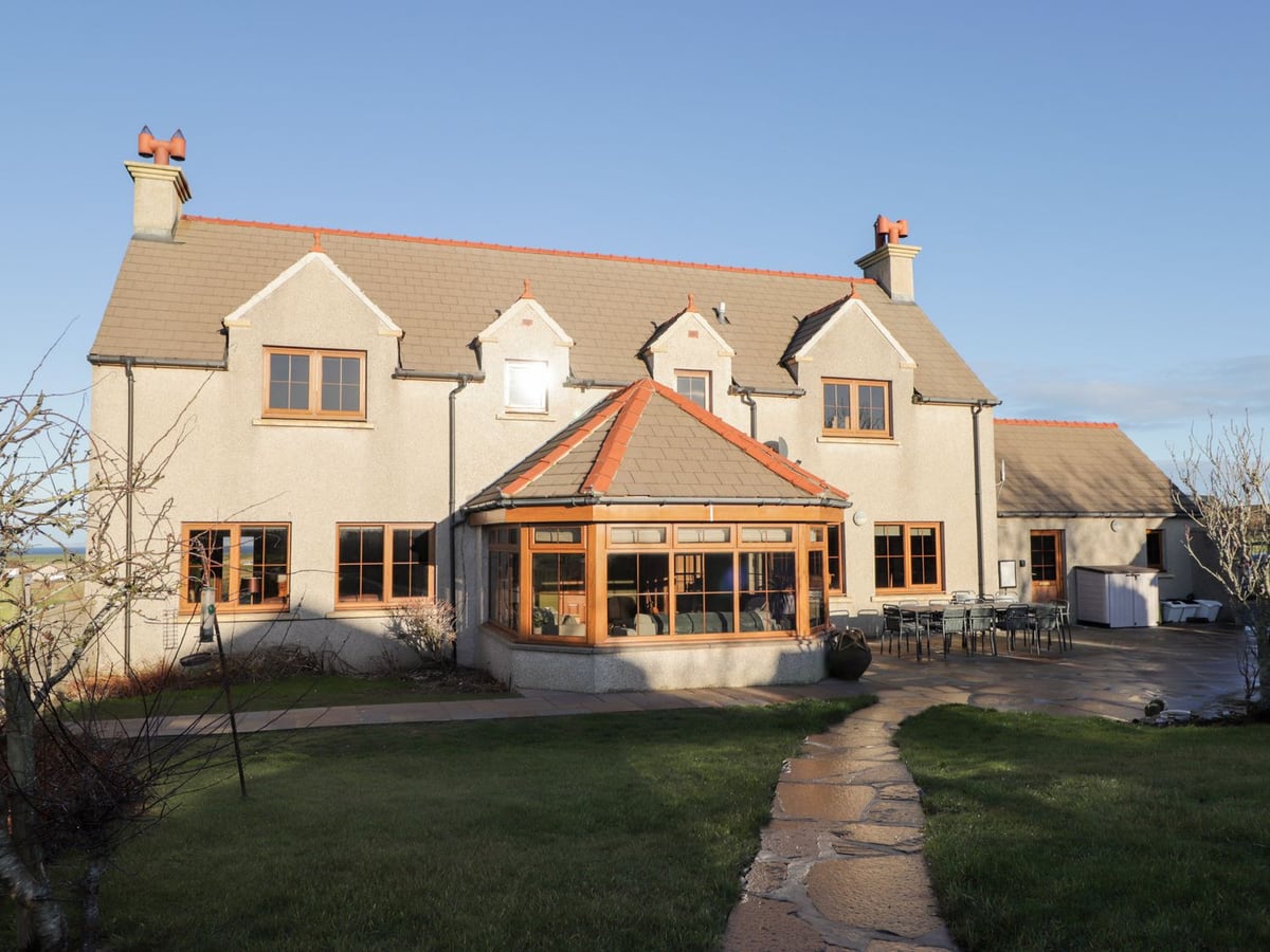 Northbanks House with a glazed sunroom, lawn path and outdoor dining table on the patio