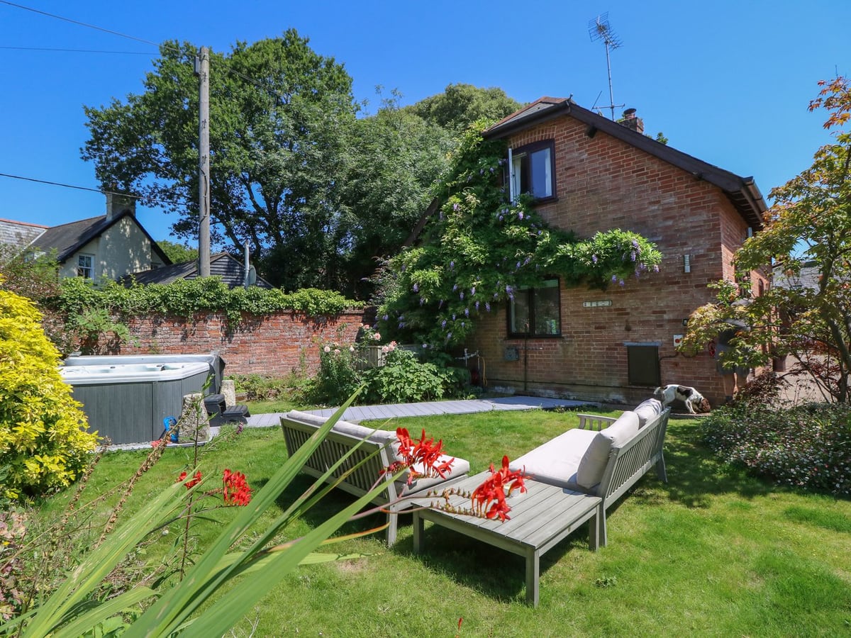 Northern Byre garden with hot tub, outdoor seating and a dog beside the brick house