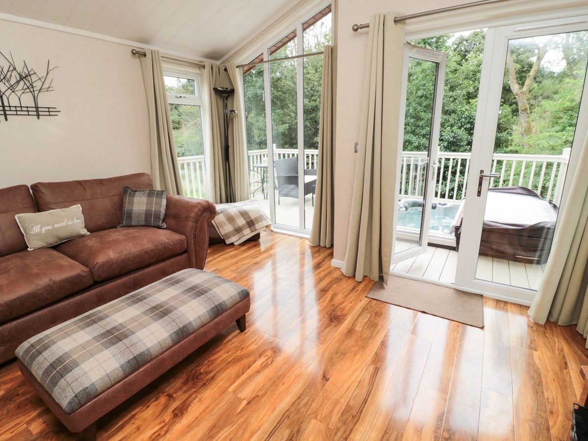 Living room at Number 43 Burnside Lodge, opening onto a deck with seating and a hot tub.