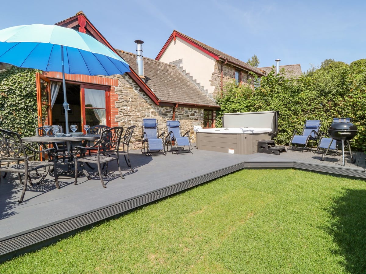 Stone cottage beside lawn and decking with a dining table and hot tub at Oak Cottage