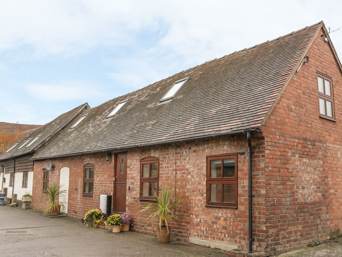 Old Hall Barn 4's brick exterior with wooden doors, roof windows and pots by the entrance