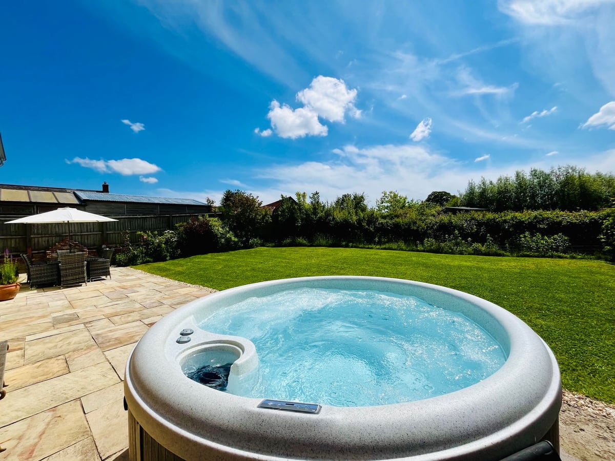 Round hot tub on the Old Post Office patio beside a lawn, hedges and outdoor dining area