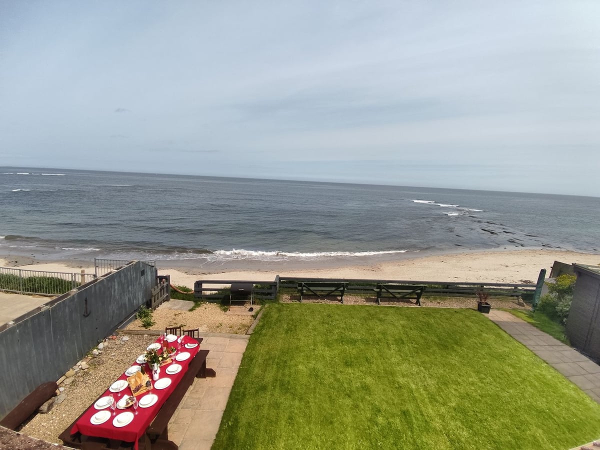 Lawn and outdoor dining at On The Watersedge, with the beach and sea beyond the boundary fence.