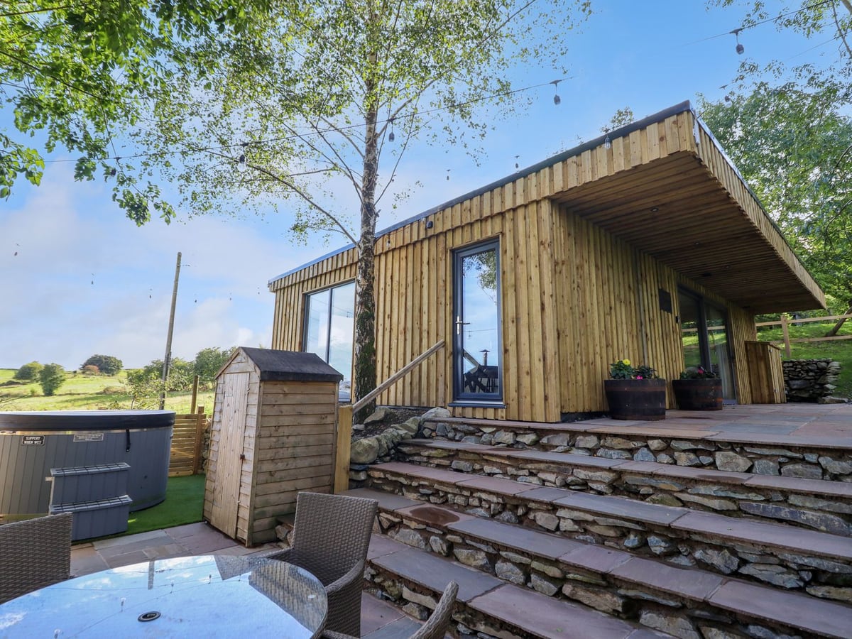 Orchard Lodge timber cabin with stone steps, a patio table and a hot tub with its lid on
