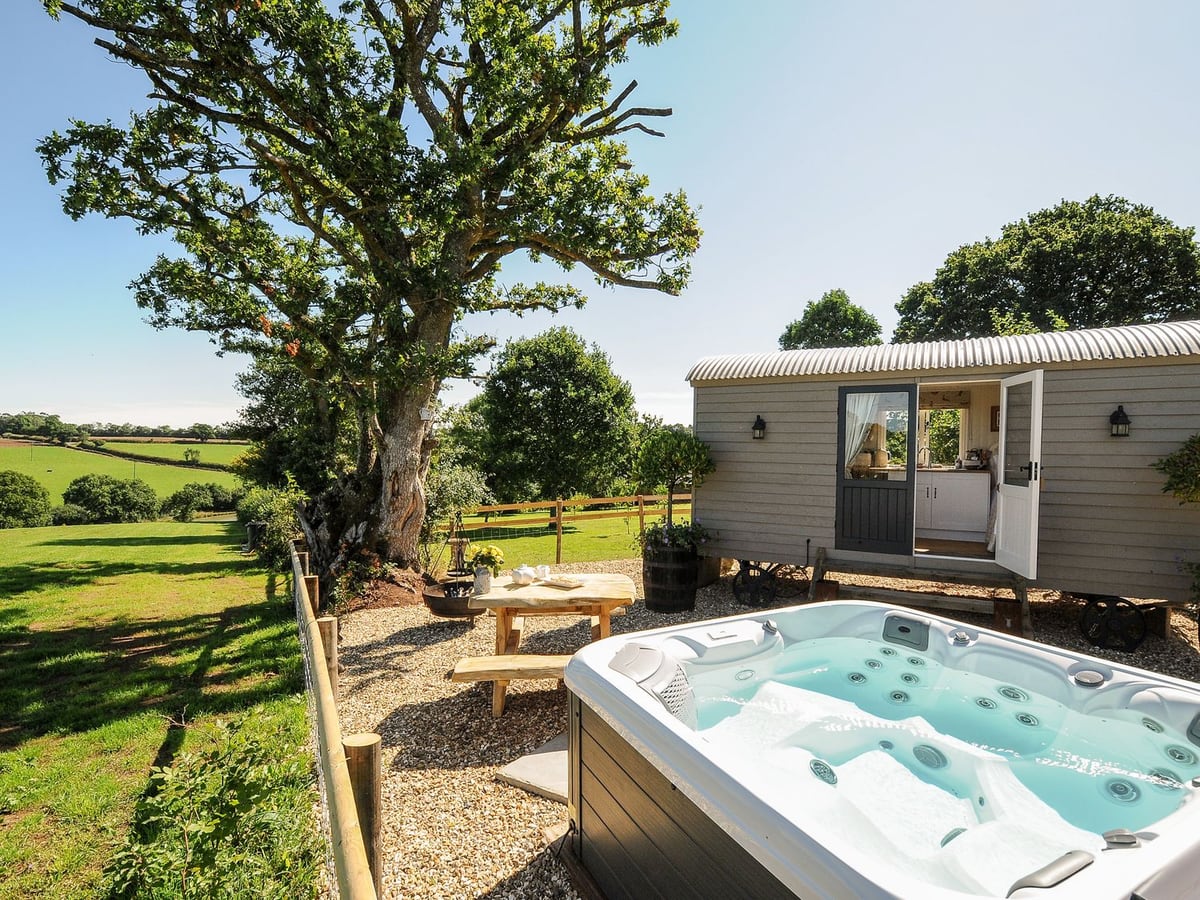 Hot tub beside the pale shepherd hut, gravel seating and open fields at Orchard Retreat