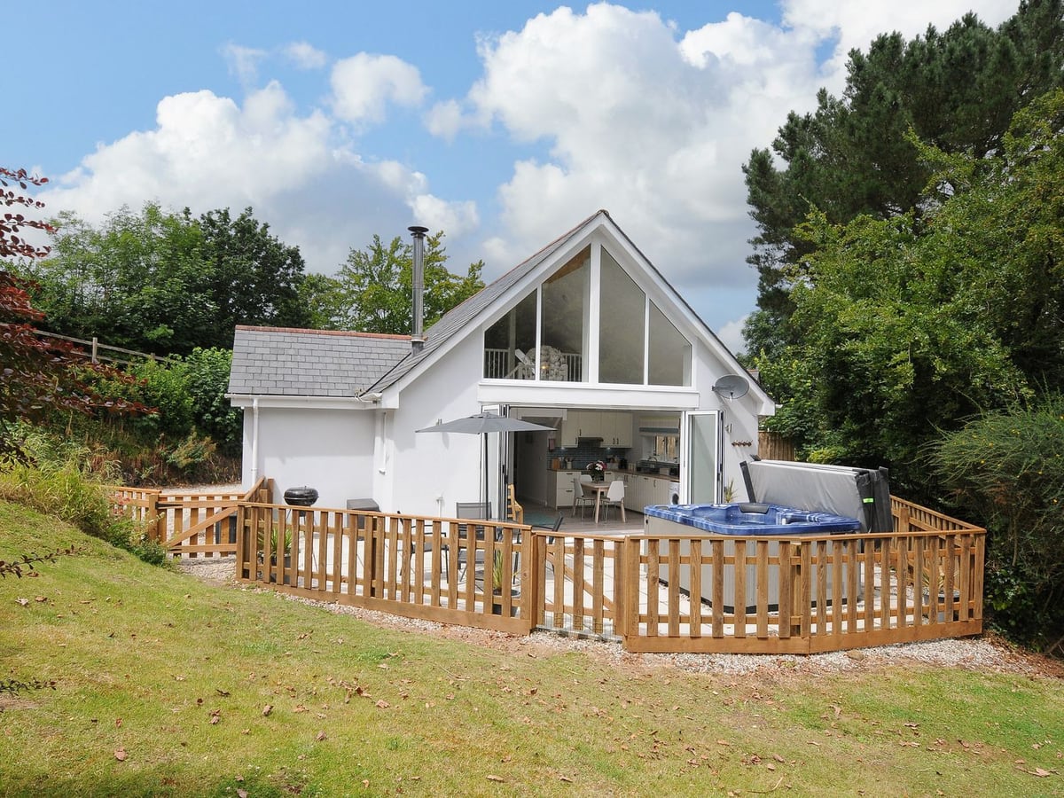 White gabled cottage with tall windows and a timber-railed terrace at Otters Leap